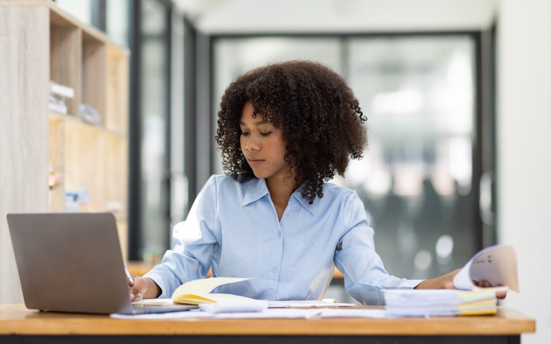 An African-American woman with natural hair sits at a desk in an office and does taxes.