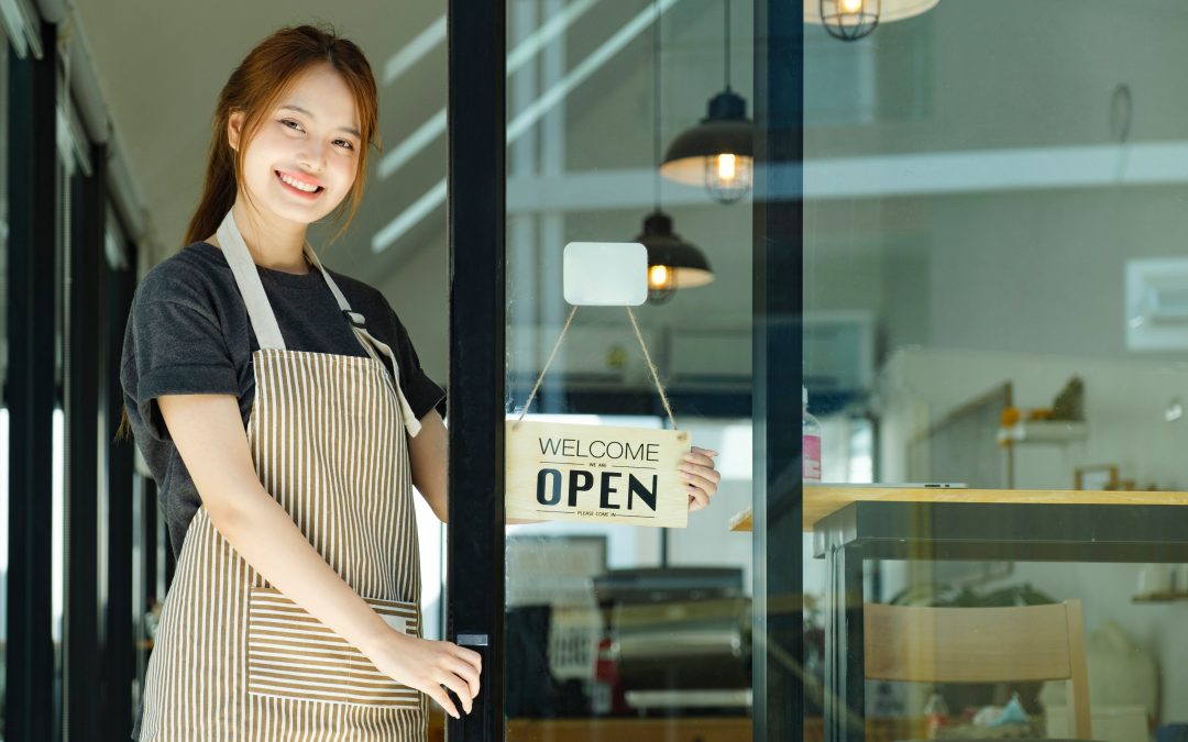 A business owner holding an "OPEN" sign on the door to her business.